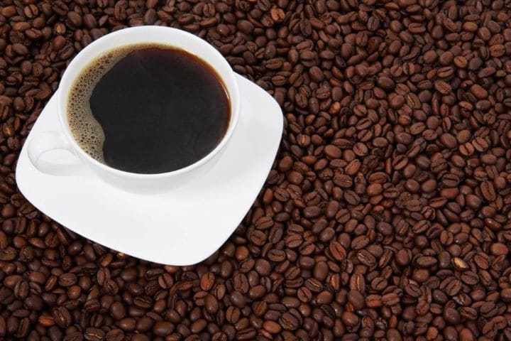 Чашка черного кофе на столе усыпанном зернами
