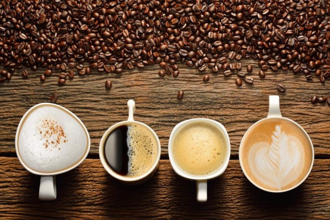 Четыре чашки с разными видами кофе и кофейные зерна на столе