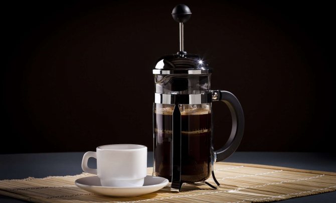French press with a cup of coffee on a black background