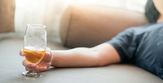 man sleeping on the sofa with a glass of alcohol in his hand